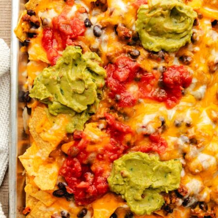 Sheet pan nachos in a rimmed baking sheet topped with guacamole and salsa.
