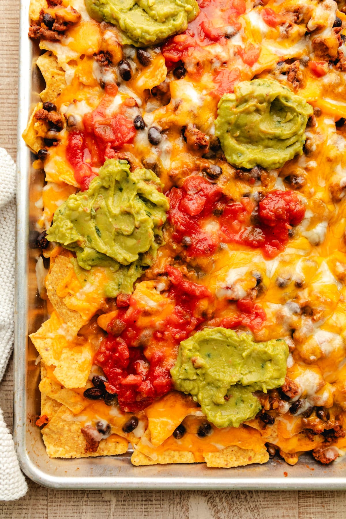 Sheet pan nachos in a rimmed baking sheet topped with guacamole and salsa.