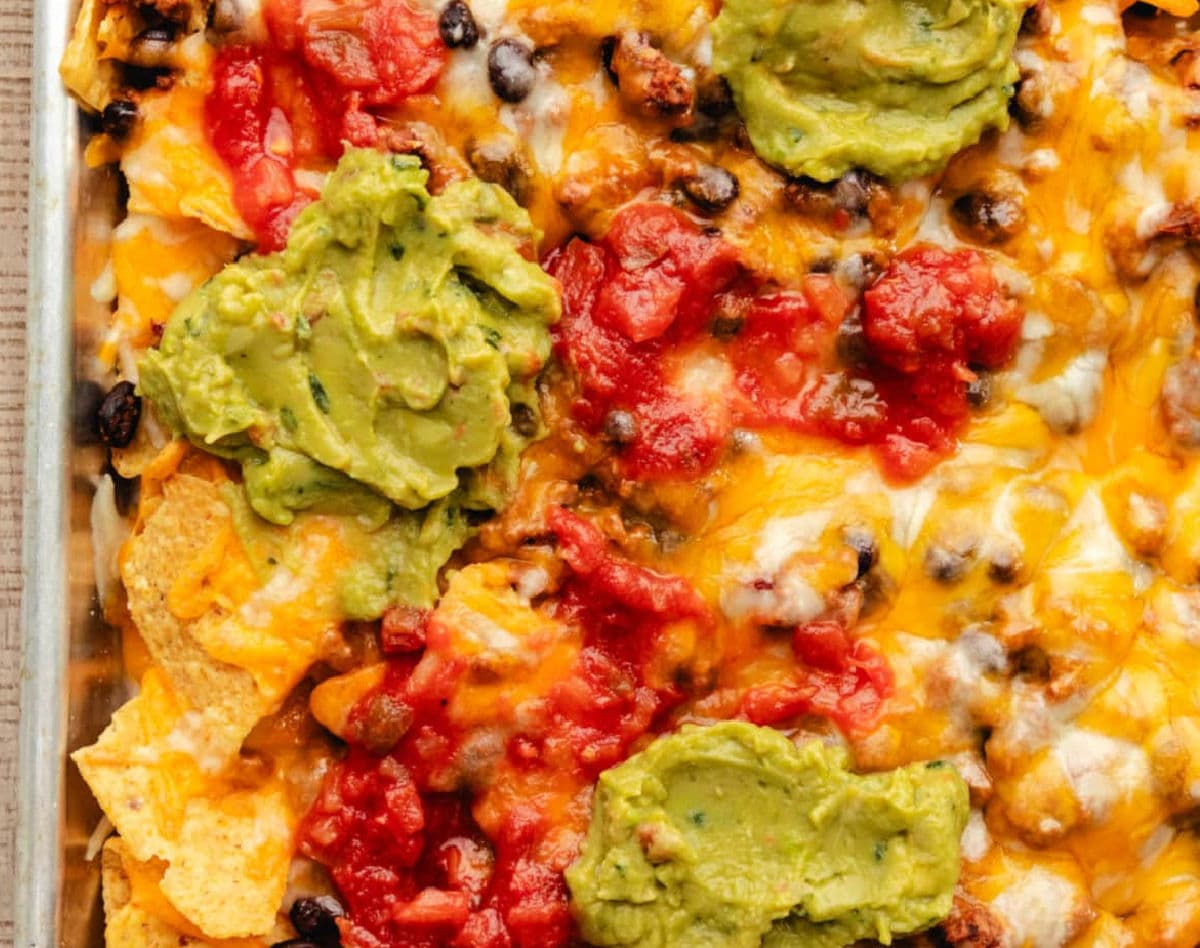 close up of sheet pan nachos topped with salsa and guacamole.
