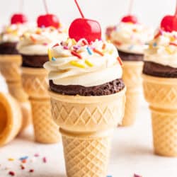 Ice cream cone cupcakes topped with vanilla frosting sprinkles and a cherry.