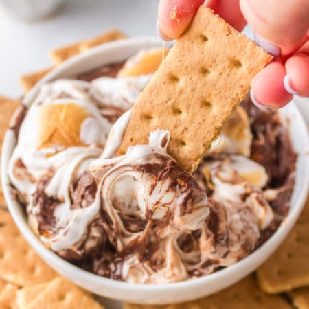 A graham cracker pulling up s'mores dip from a dish.