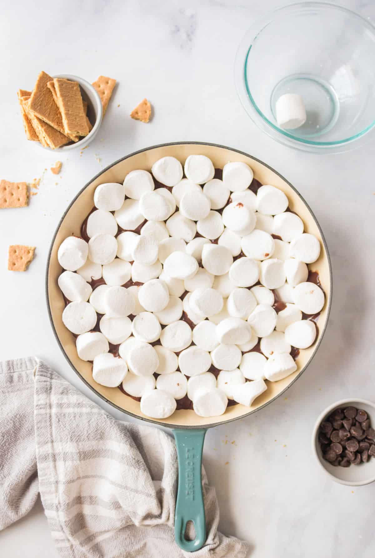 Marshmallows on top of chocolate chips in a cast iron skillet.