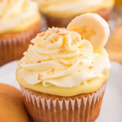 A banana pudding cupcake on a white plate next to a nilla wafer.