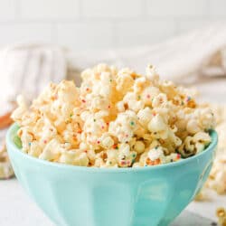 A teal dish of birthday cake popcorn next to pieces of popcorn.