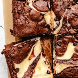 A cut cheesecake brownie slightly at an angle next to the brownies.