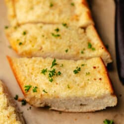 Sliced homemade garlic bread on brown parchment paper.