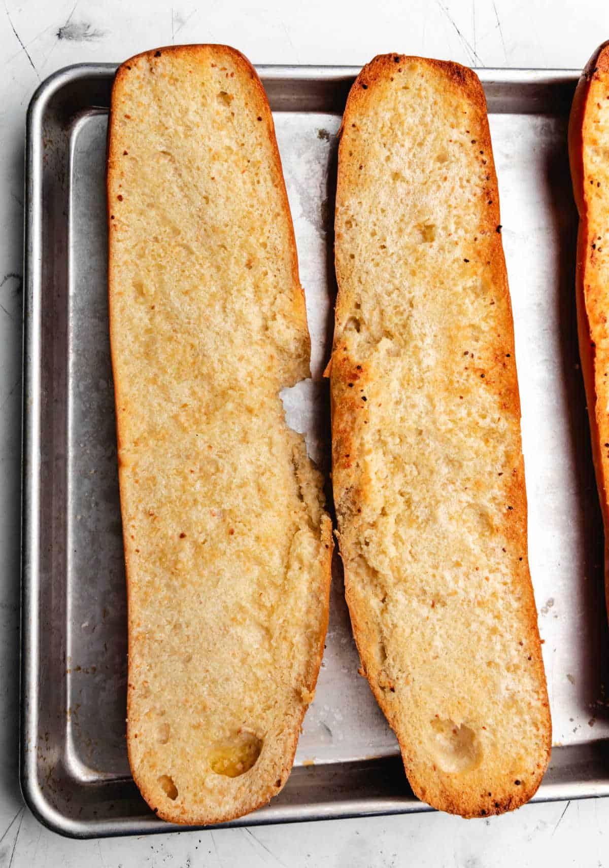 Two halves of baked garlic bread on a baking tray.