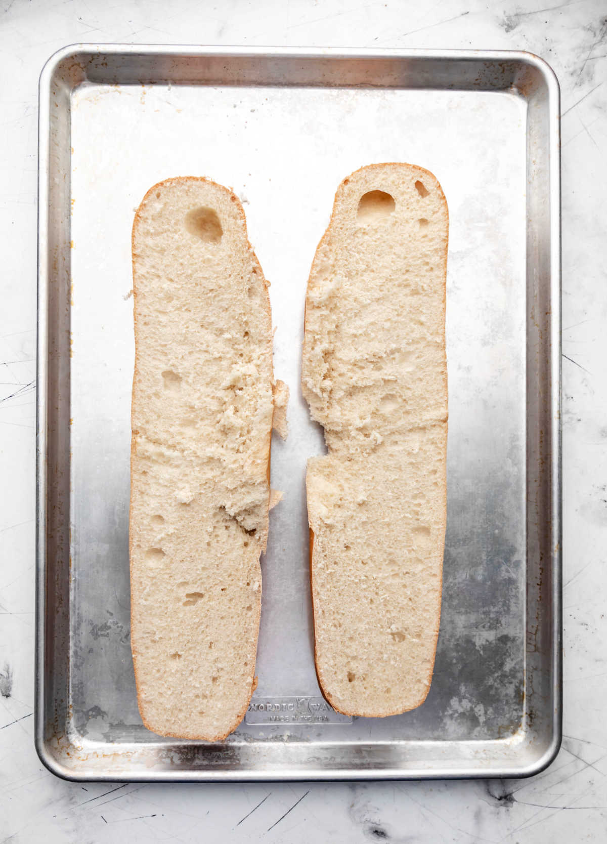 A loaf of French bread sliced in half on a rimmed baking sheet.
