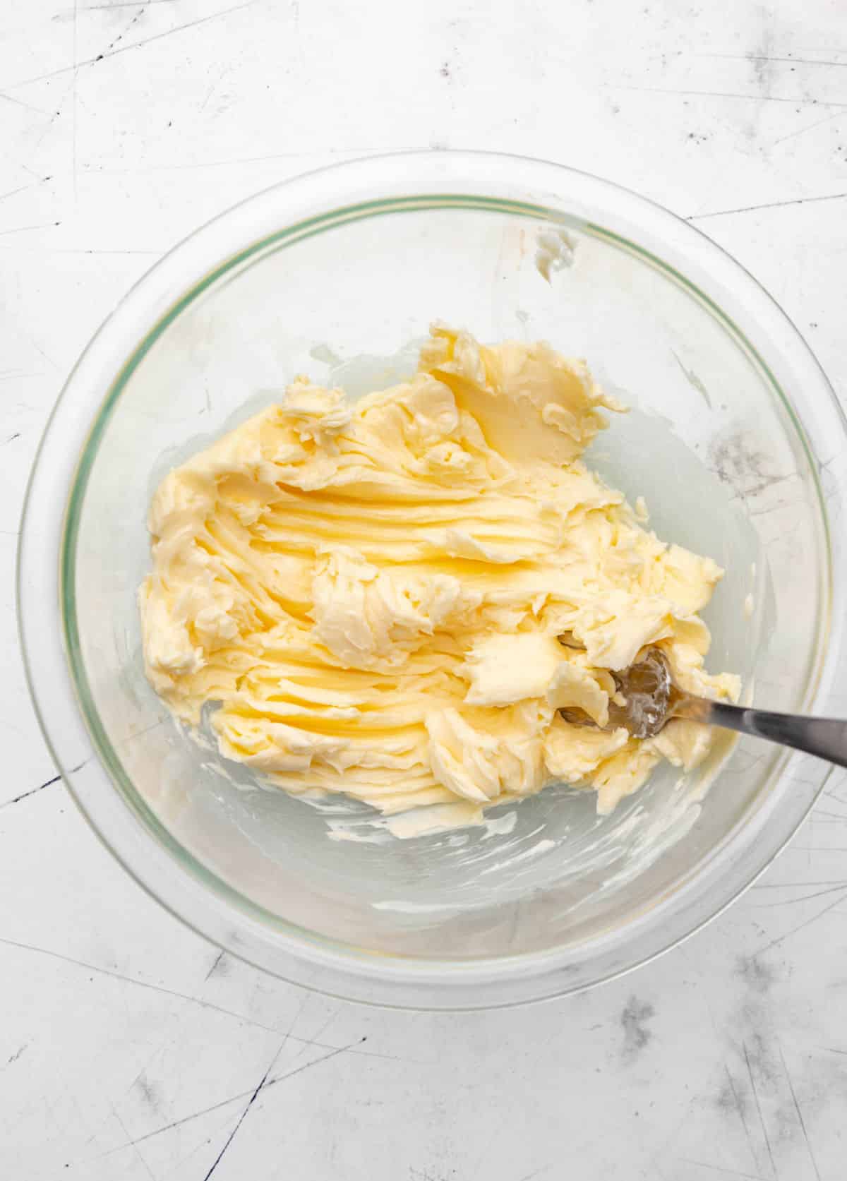 A fork mixing butter in a glass mixing bowl.
