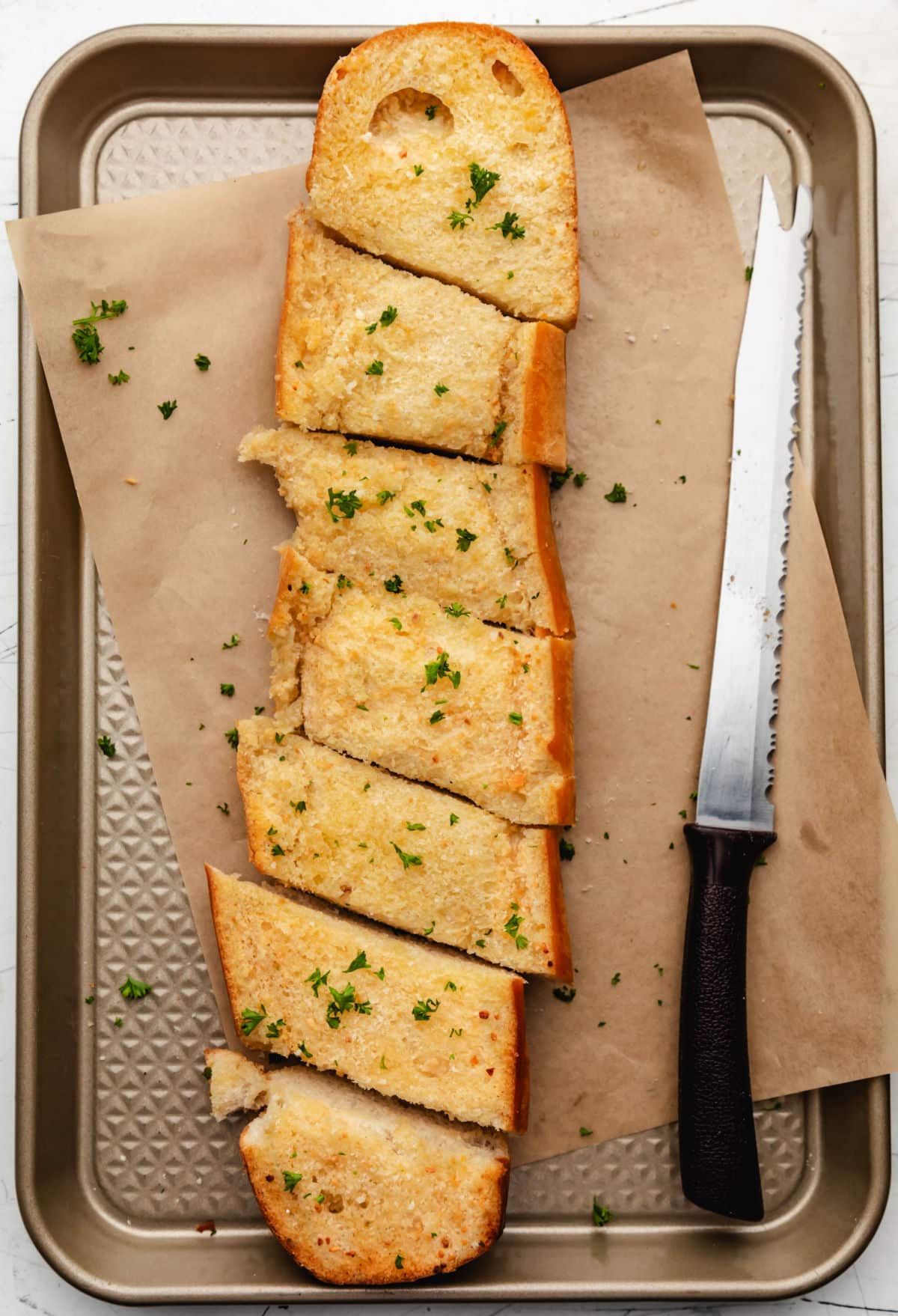 Sliced baked homemade garlic bread on a baking tray.