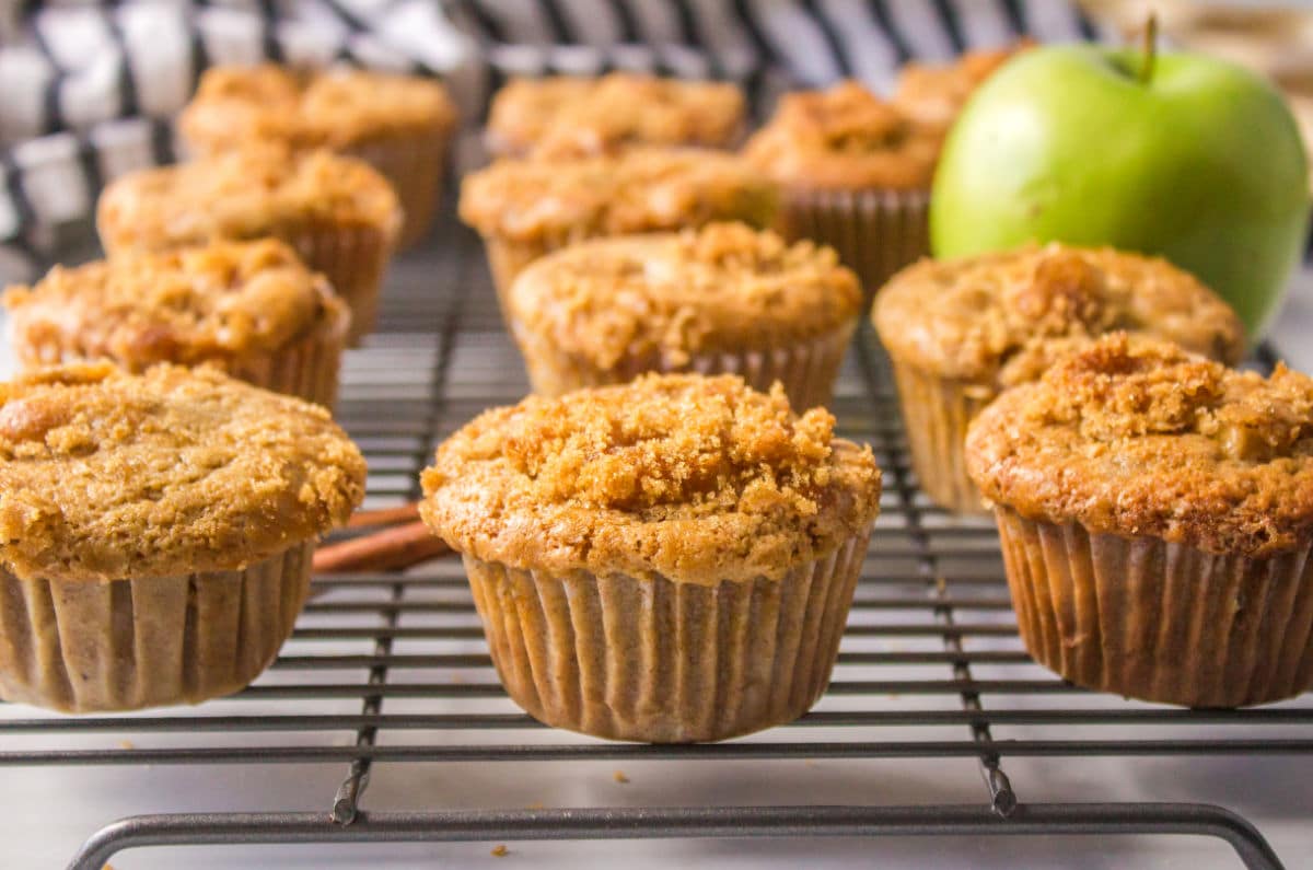Apple muffins a green apple and cinnamon sticks on a wire cooling rack.