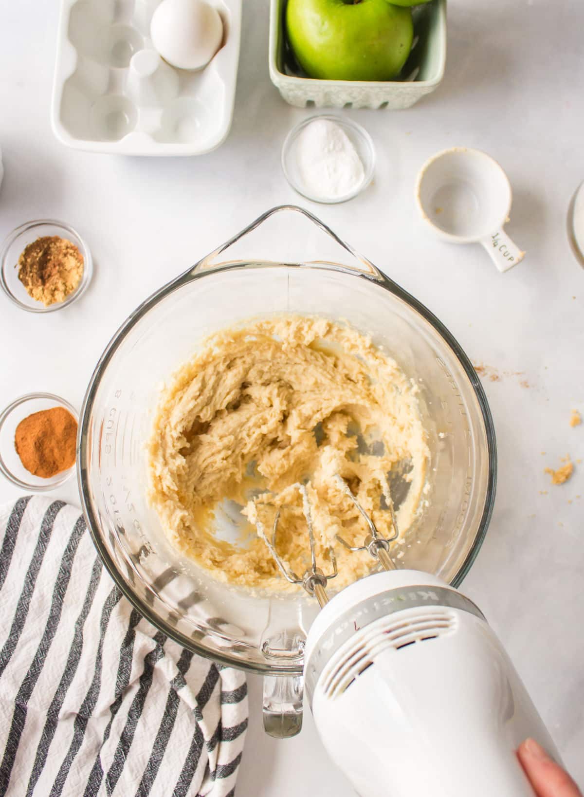 A hand mixer creaming butter and sugar together in a glass mixing bowl.