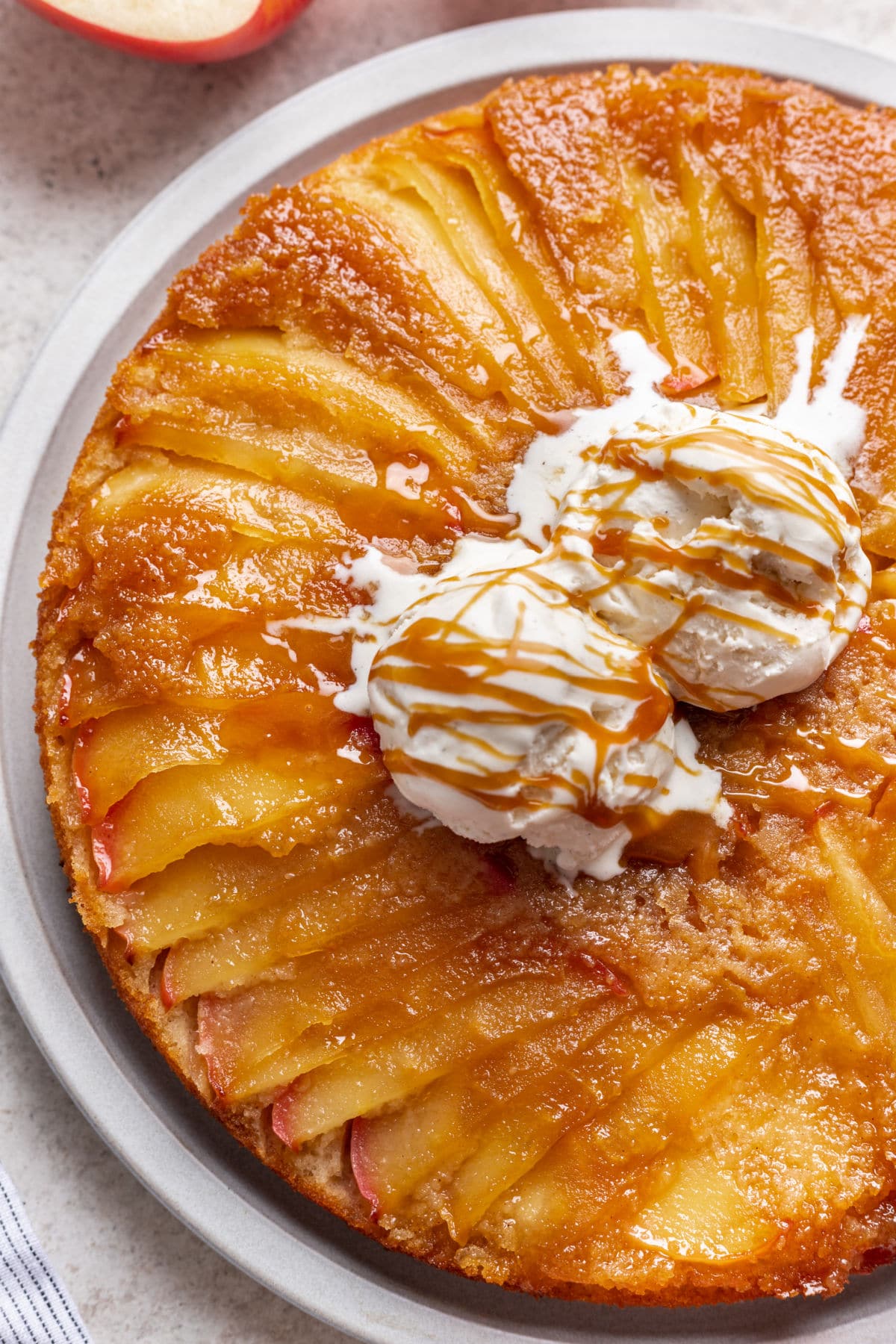 Close up photo of apple upside down cake with vanilla ice cream and caramel sauce on top.
