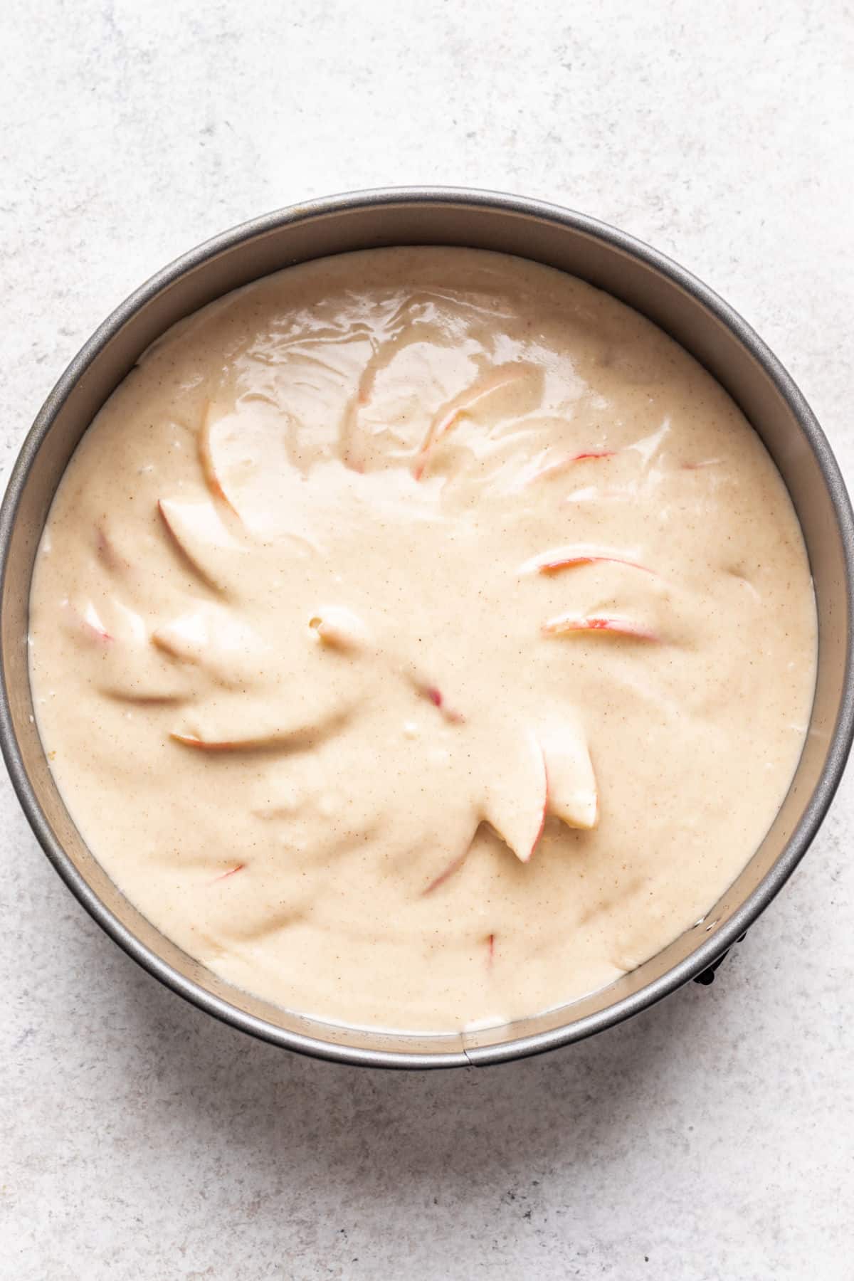Batter over apple slices in a cake pan.