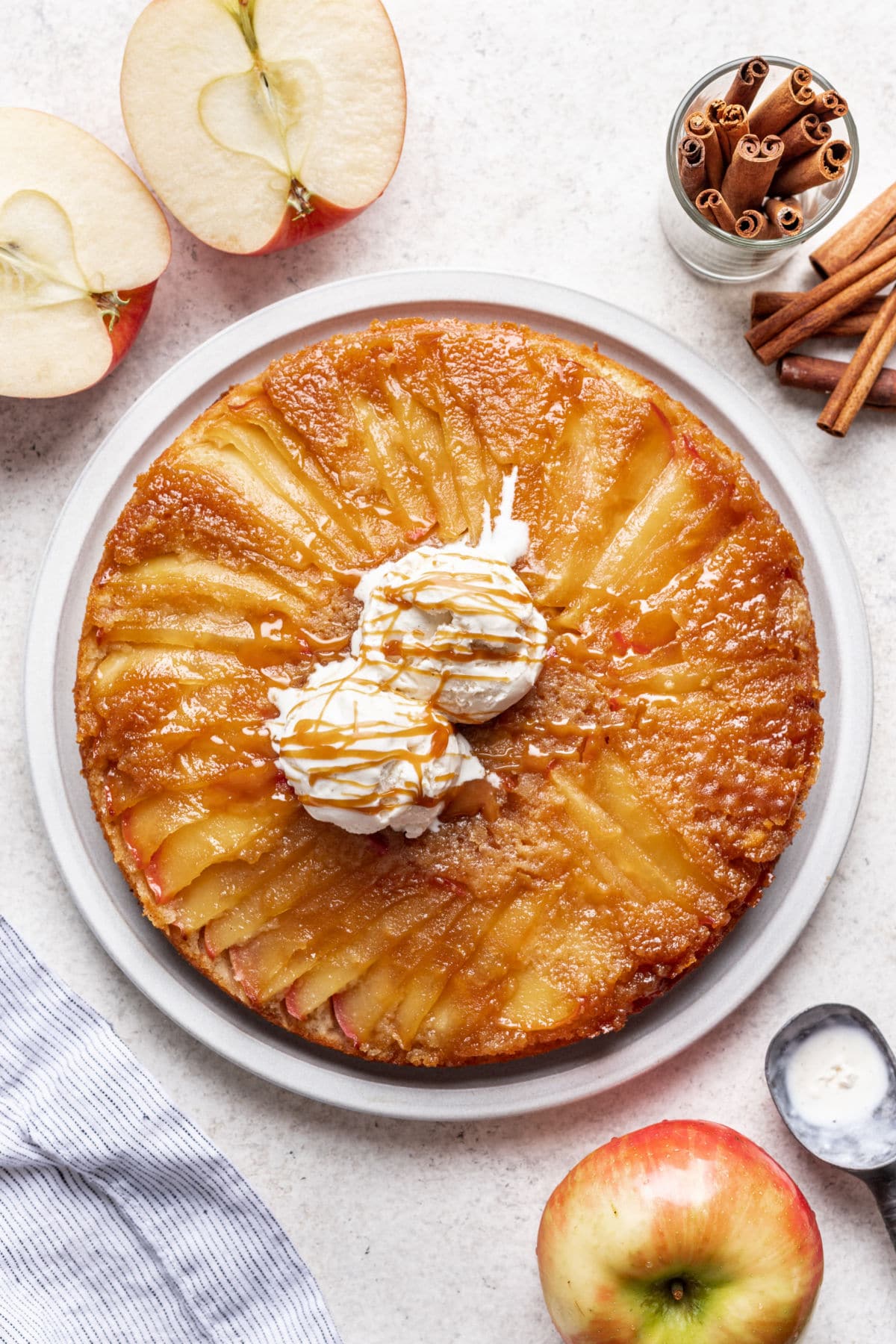 An apple upside down cake next to apples and cinnamon sticks.