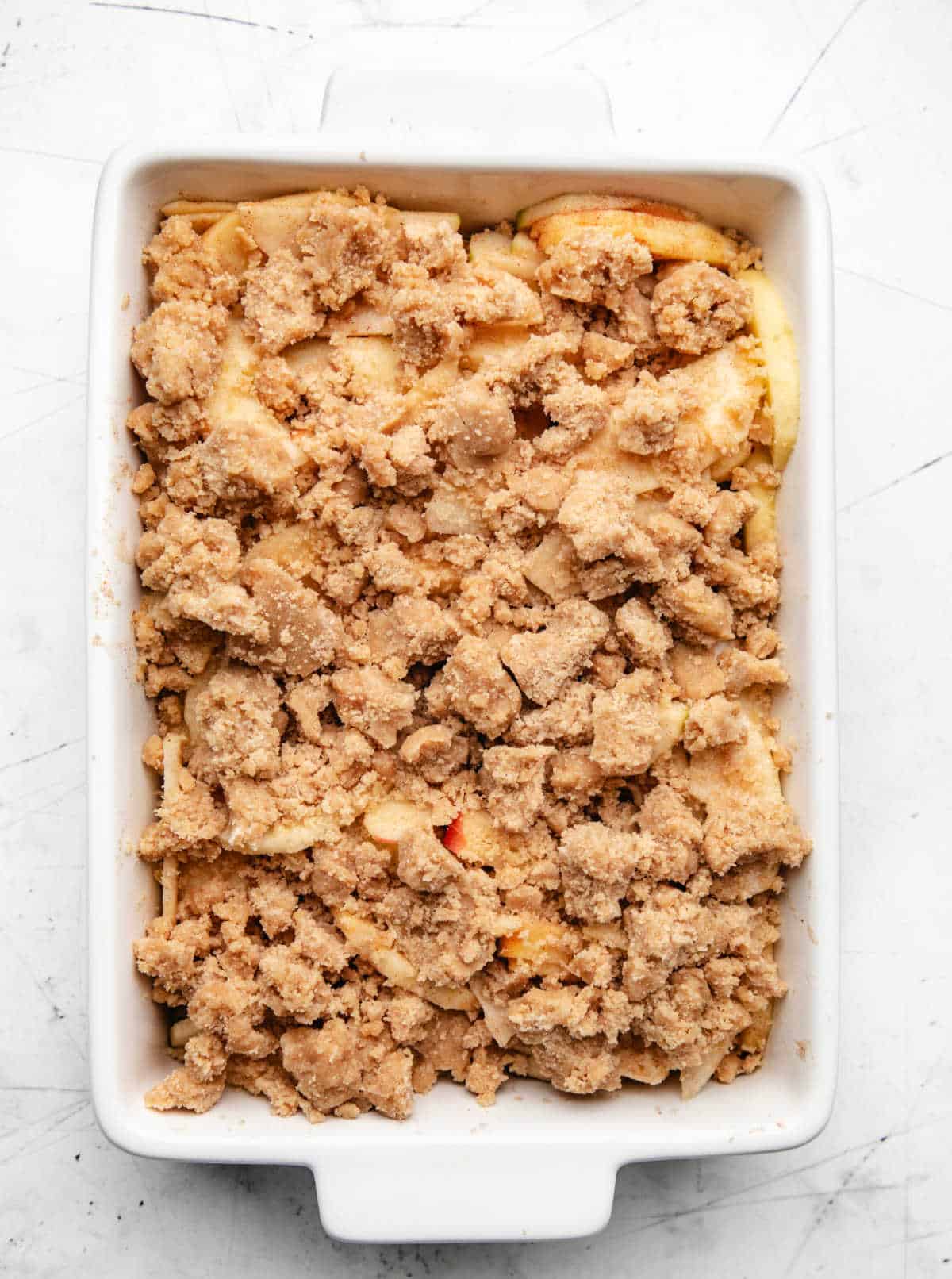 Unbaked crumble topping over apple filling in a baking pan.