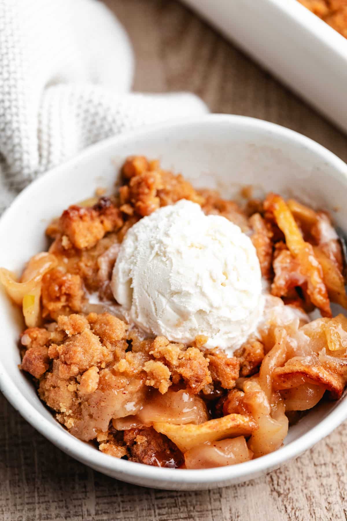 A scoop of vanilla ice cream on top of a bowl of apple crumble.