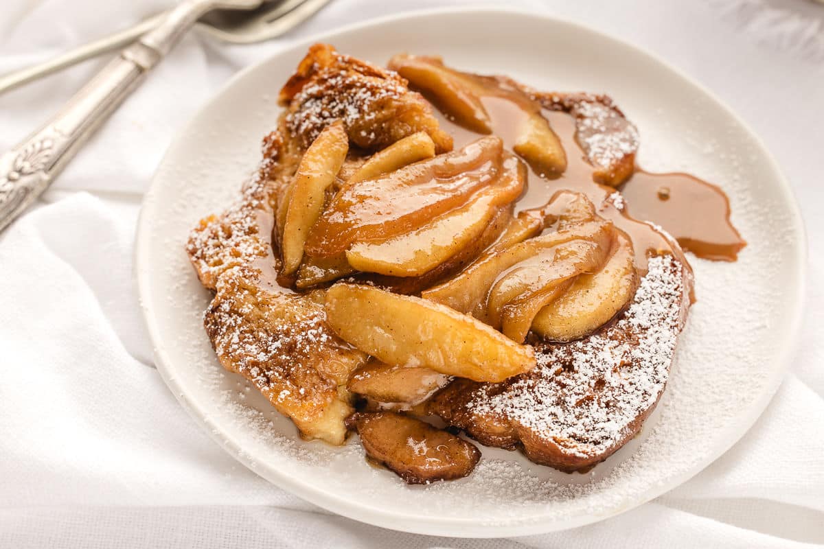 A white plate of apple baked French toast topped with powdered sugar.