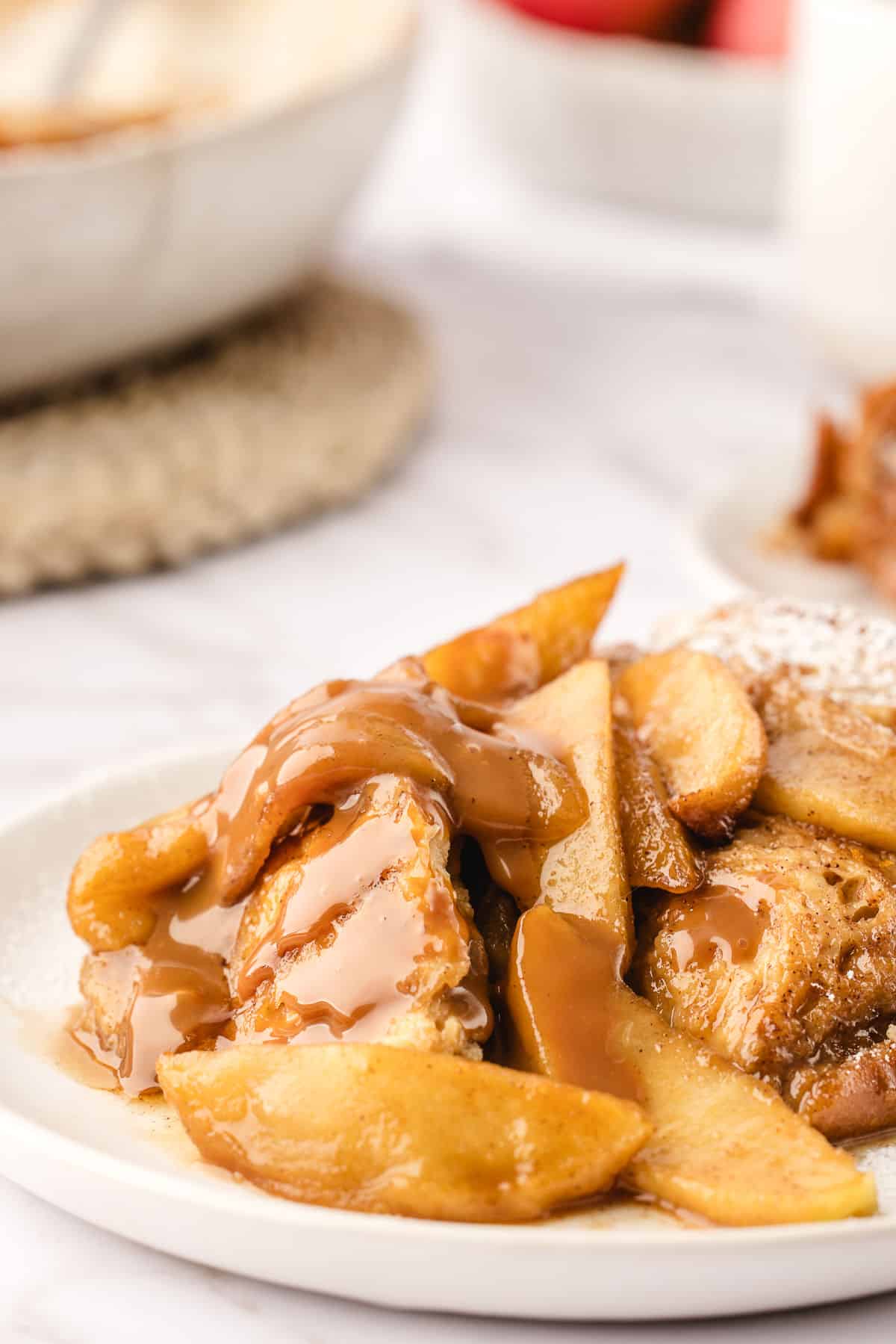 A white plate with apple baked French toast next to the dish of French toast.