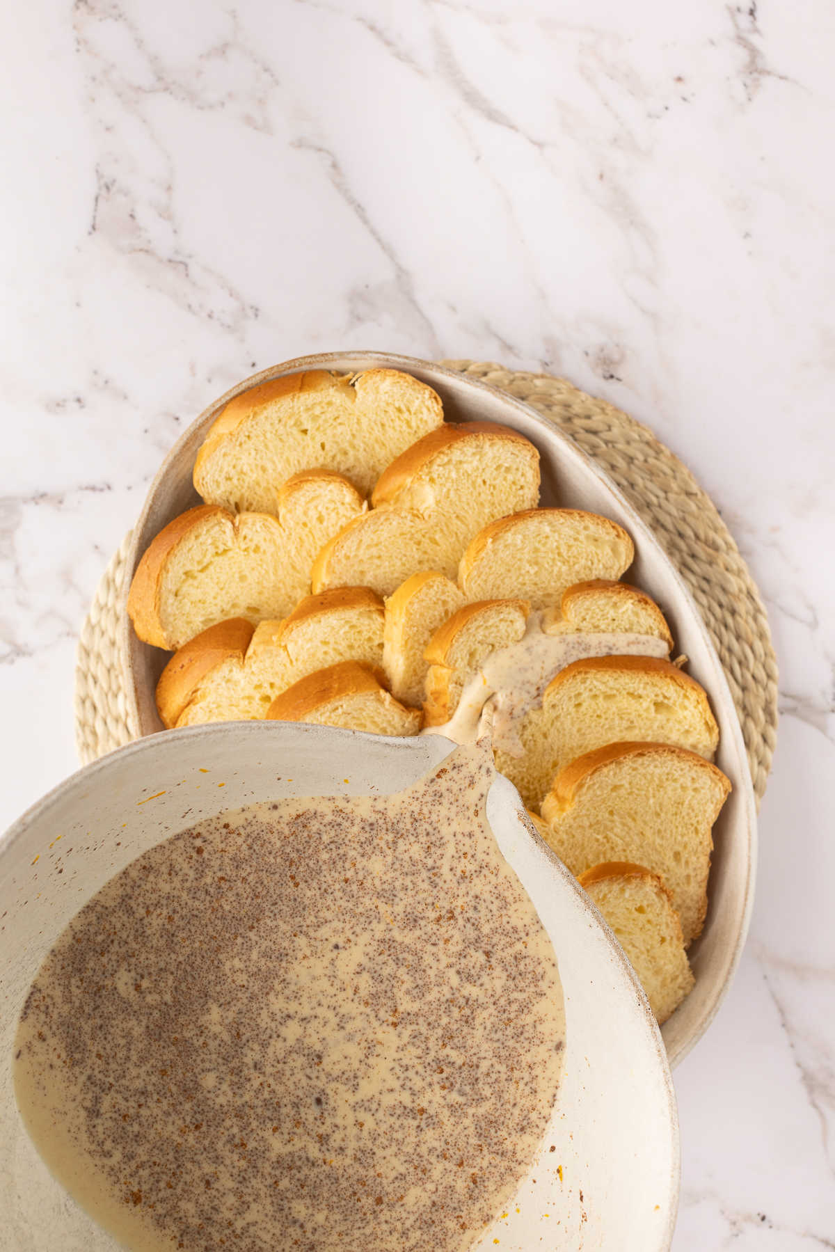 Custard pouring over slices of brioche bread in an oval baker.