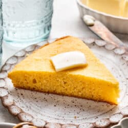 A slice of homemade cornbread topped with a pat of butter on a plate.