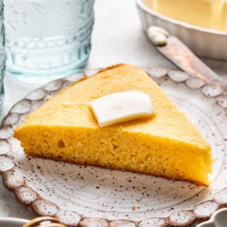 A slice of homemade cornbread topped with a pat of butter on a plate.