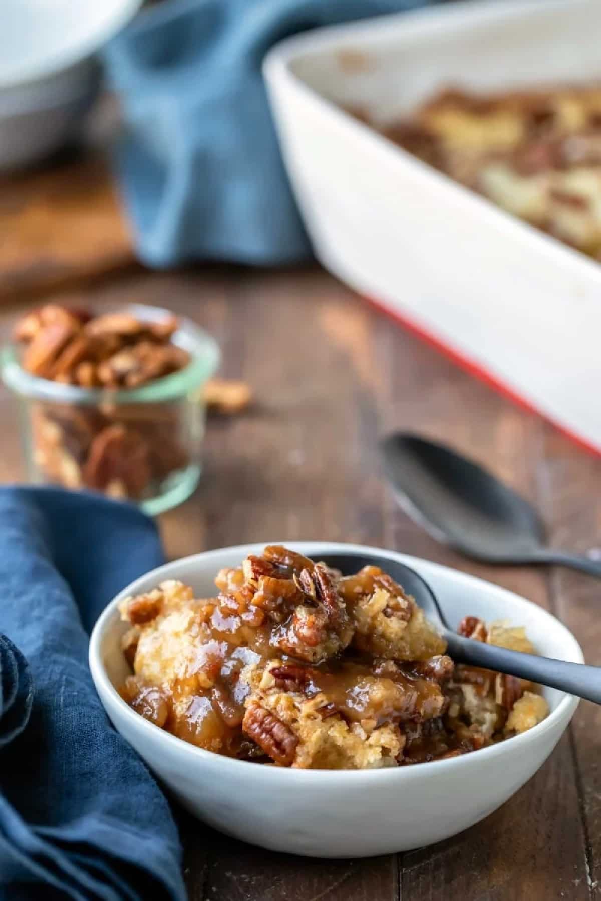 A dish of pecan pie pudding cake next to a dish of pecans.