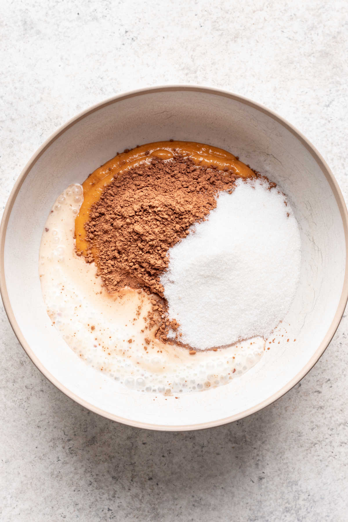 Cocoa powder buttermilk and sugar on pumpkin batter in a mixing bowl.