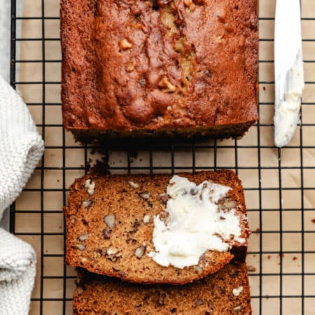 A partially buttered slice of date nut bread next to the loaf of date bread.