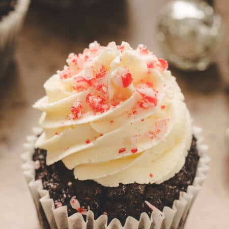 A chocolate peppermint cupcake next to a silver jingle bell.