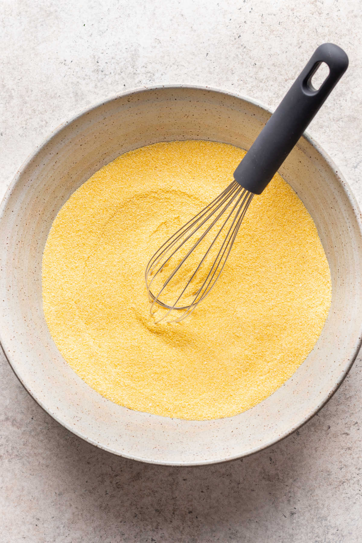 Dry ingredients for cornbread whisked together in a mixing bowl.