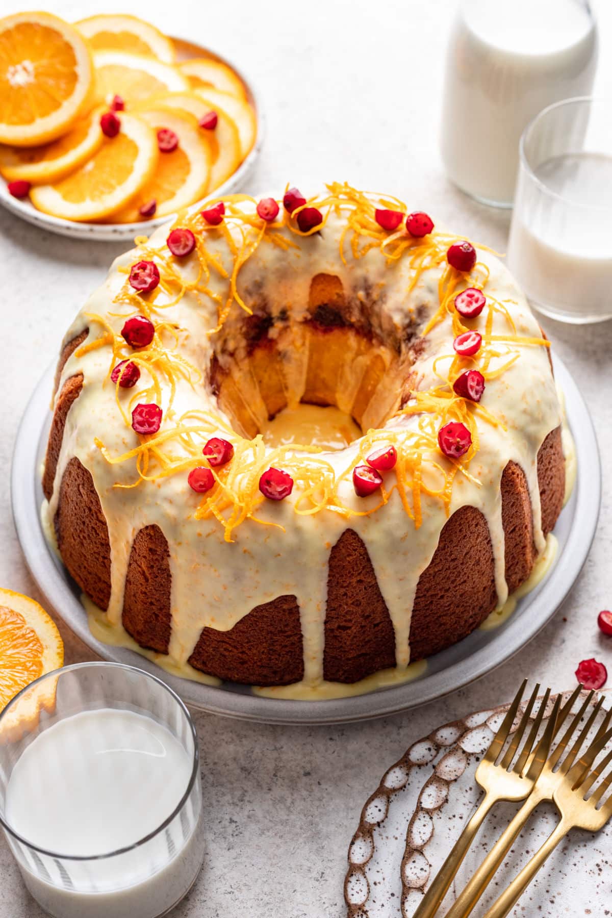 An iced cranberry orange pound cake on a platter topped with fresh orange zest and cranberries.
