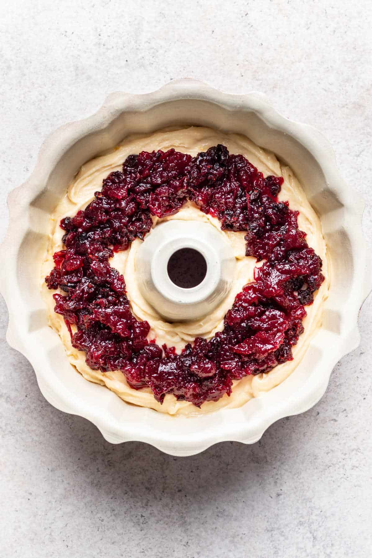 A layer of cranberry sauce on top of cranberry orange pound cake batter in a bundt pan.