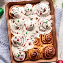 A pan of partially frosted cinnamon rolls next to cups of coffee and a dish of frosting.