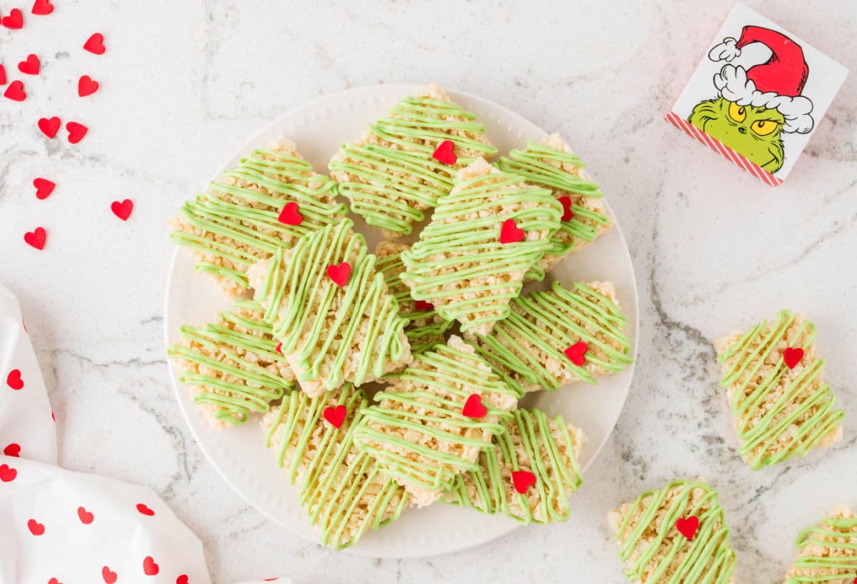 A plate of Grinch Rice Krispies treats next to scattered candy hearts.