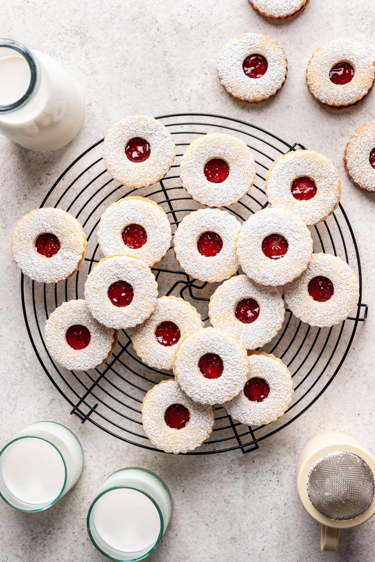 Overlapping linzer cookies on a wire cooling rack next to cups of milk.