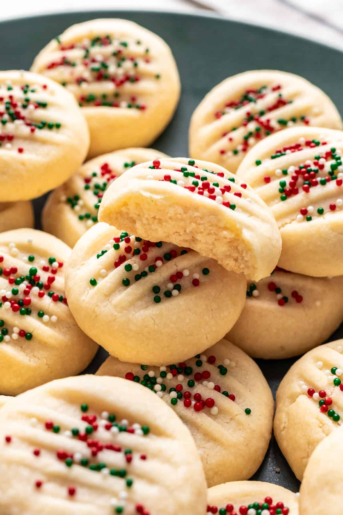A whipped shortbread cookie broken in half on top of other shortbread cookies.