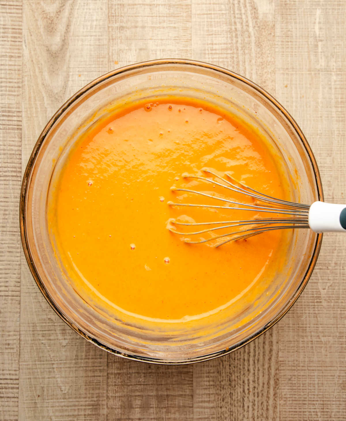 Pumpkin puree, eggs, milk, and spices whisked together in a mixing bowl.