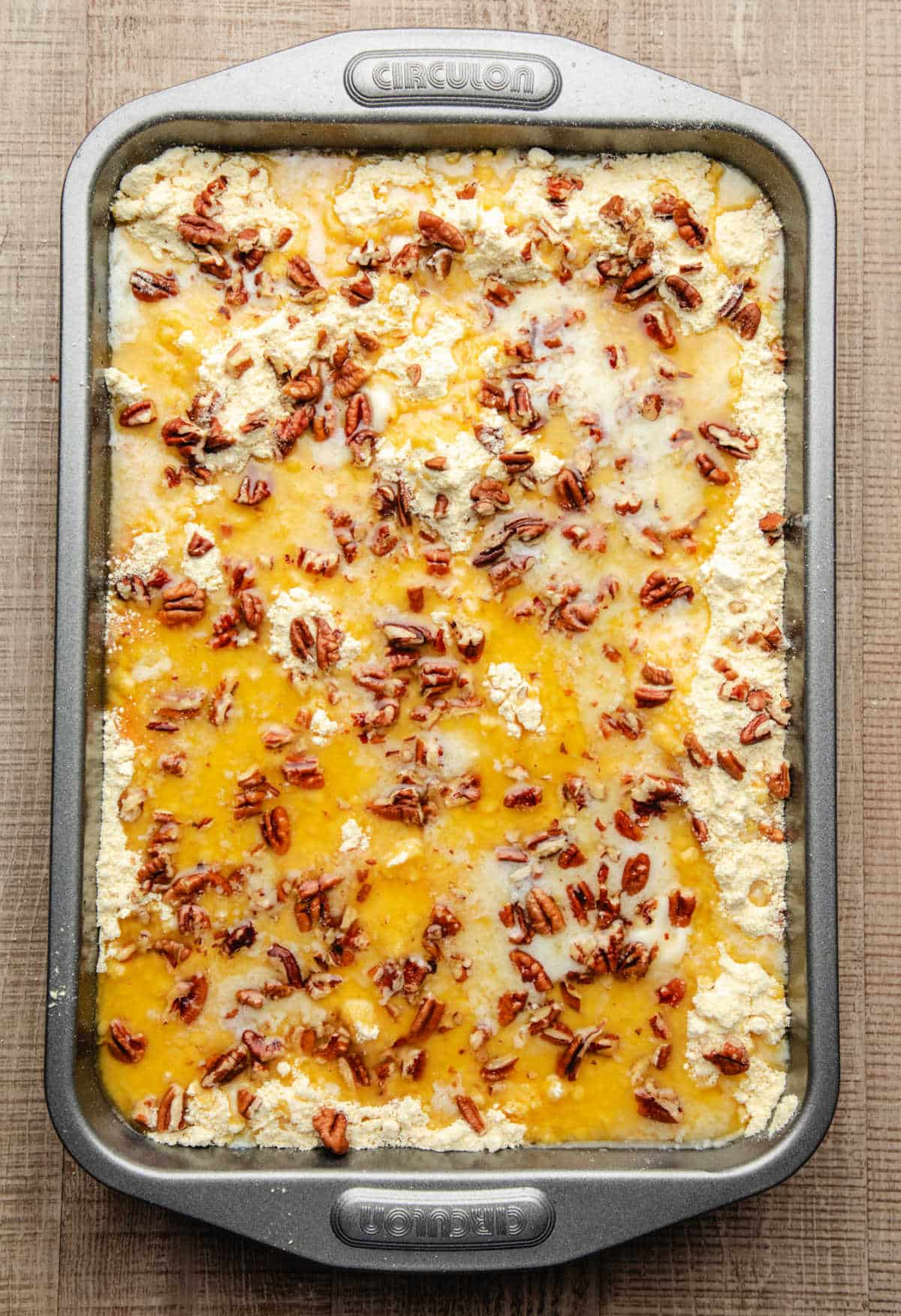 Chopped pecans on top of melted butter and cake mix in a pan.