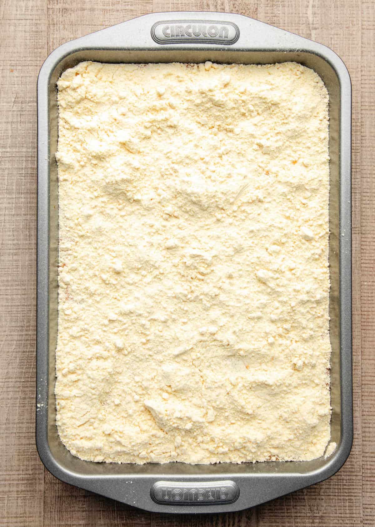 Yellow cake mix sprinkled over pumpkin pie filling in baking pan.