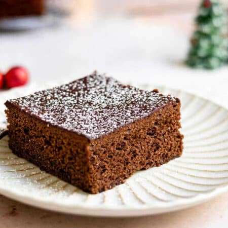 Piece of gingerbread on a white plate next to Christmas decorations.