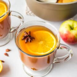 Two cups of cider wassail next to the saucepan.