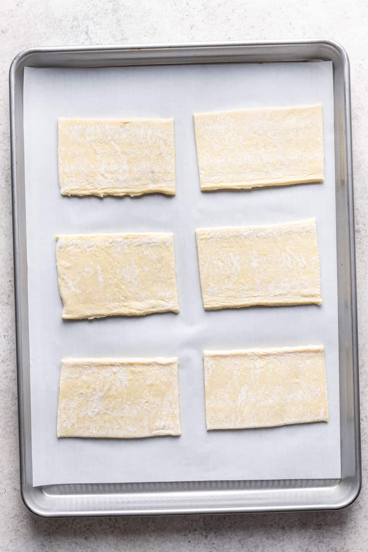 Six pieces of puff pastry dough on a baking sheet.