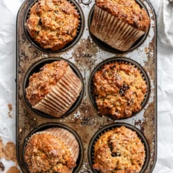 Six oatmeal raisin bran muffins in a vintage tin with the muffins at an angle.