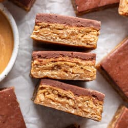 Three peanut butter bars on their side next to a dish of peanut butter.