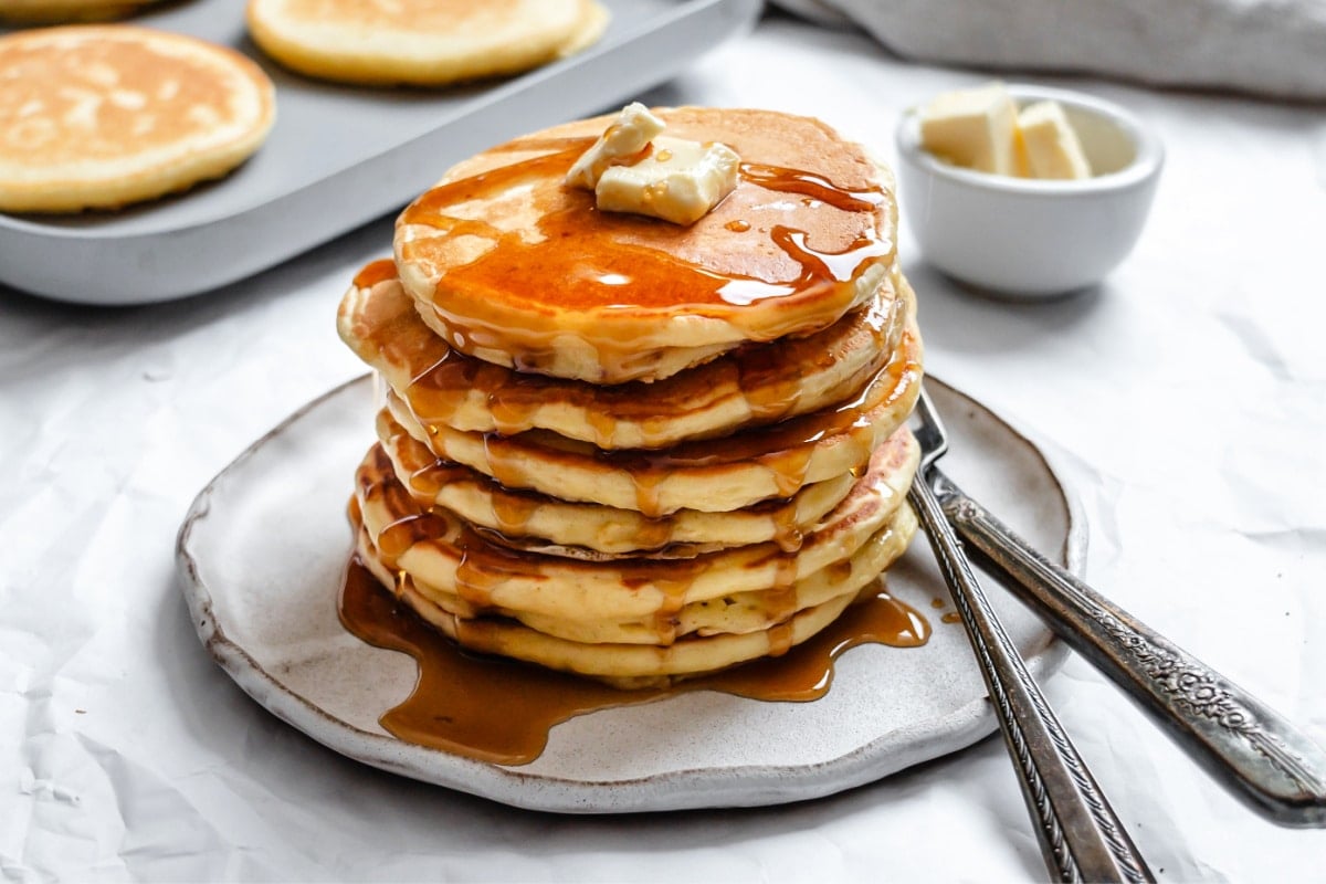 Sour Cream Pancake Recipe A stack of sour cream pancakes topped with pats of butter and maple syrup.