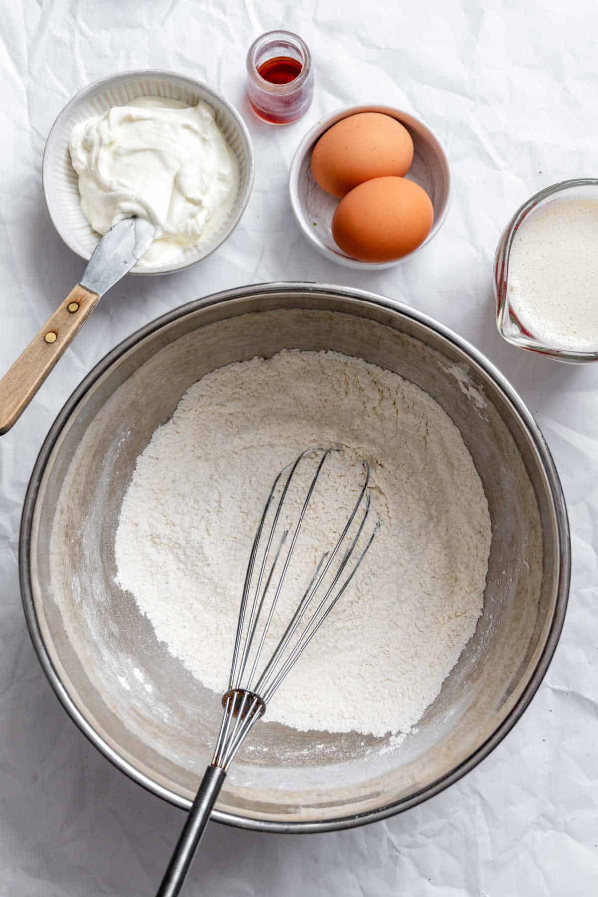 A whisk whisking dry ingredients for sour cream pancakes in a silver mixing bowl.