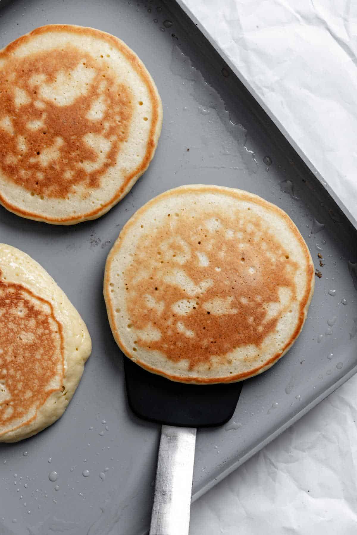 A spatula flipping pancakes on a griddle.