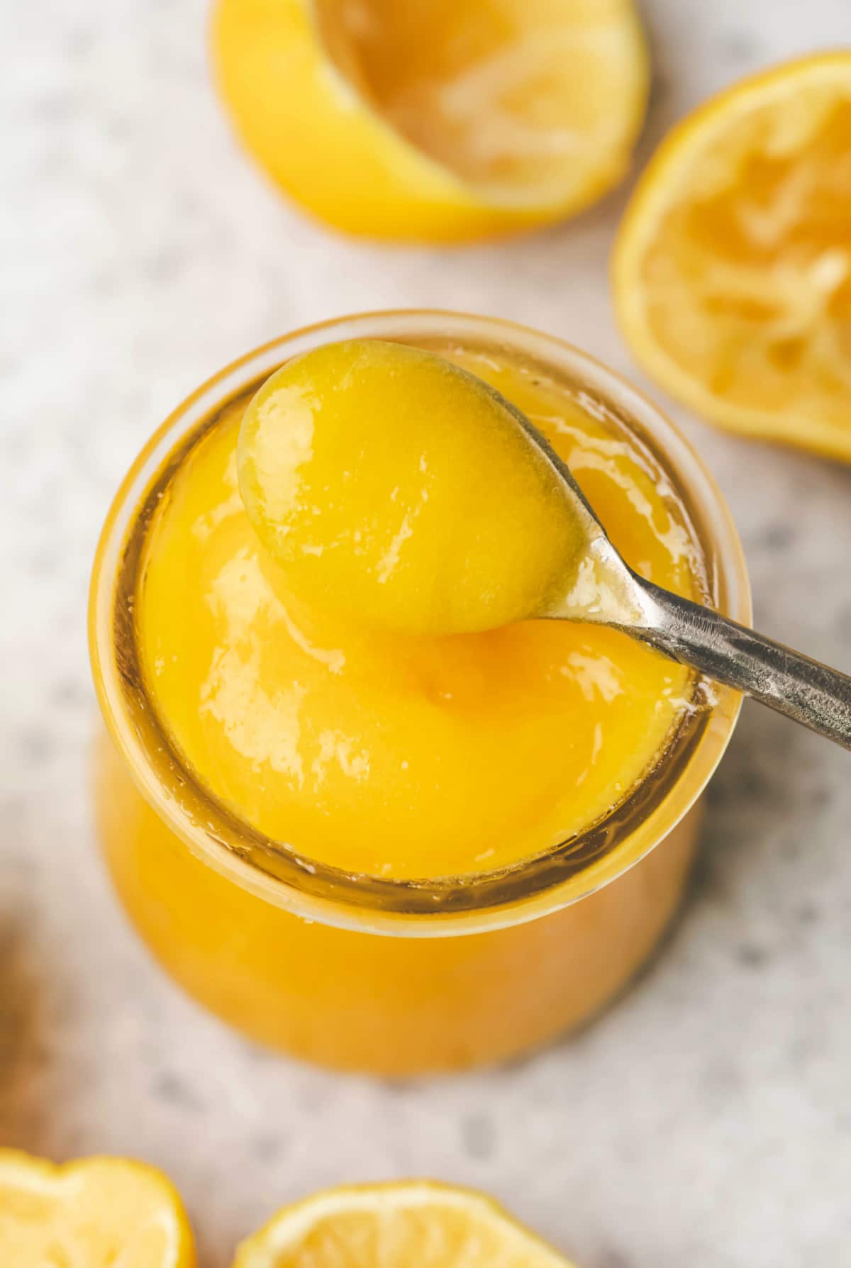 A silver spoon scooping up lemon curd from a glass jar.