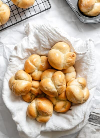 A basket of 60 minute dinner rolls next to a wire cooling rack with more rolls.